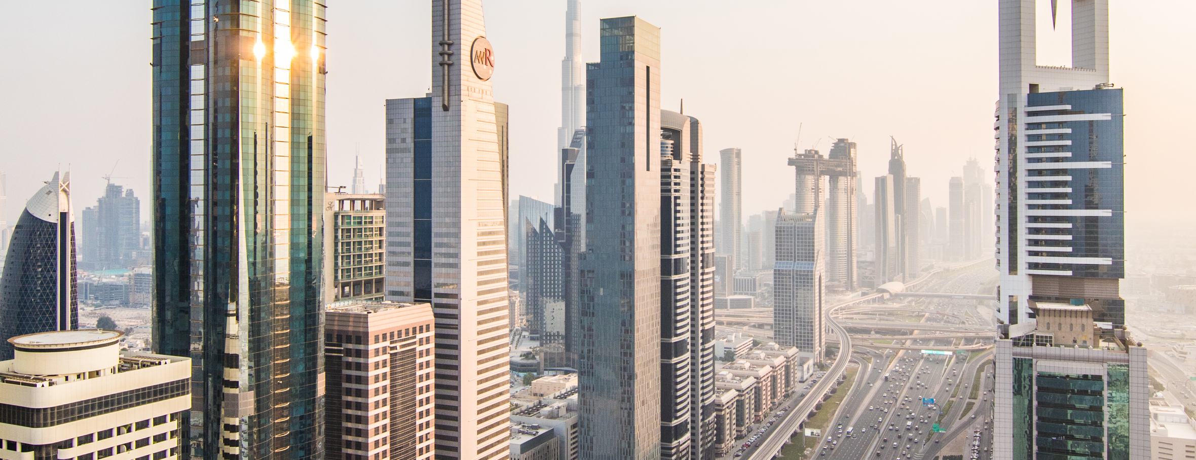 Sheikh Zayed Road at golden hour, looking toward the Burj Khalifa, with the Metro line and traffic below